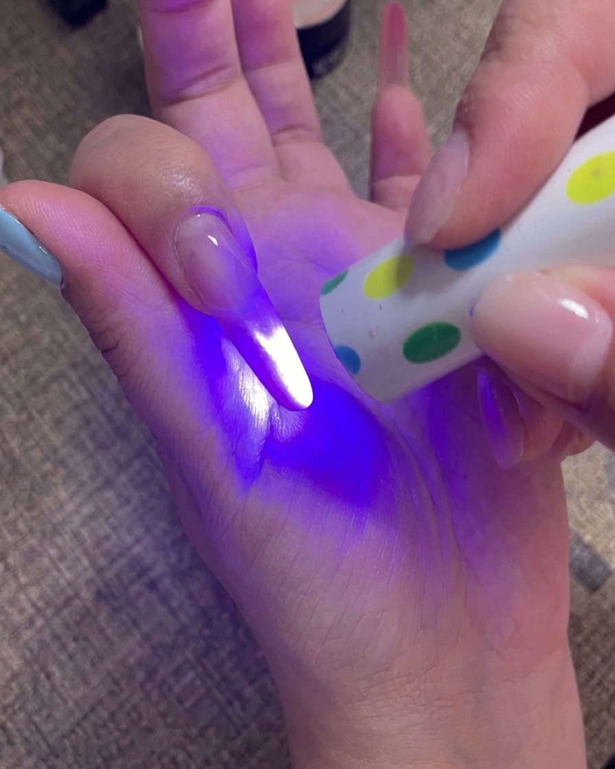 Eine Hand hält eine tragbare UV-Lampe direkt über die Fingernägel, um die letzte Gelschicht auszuhärten.