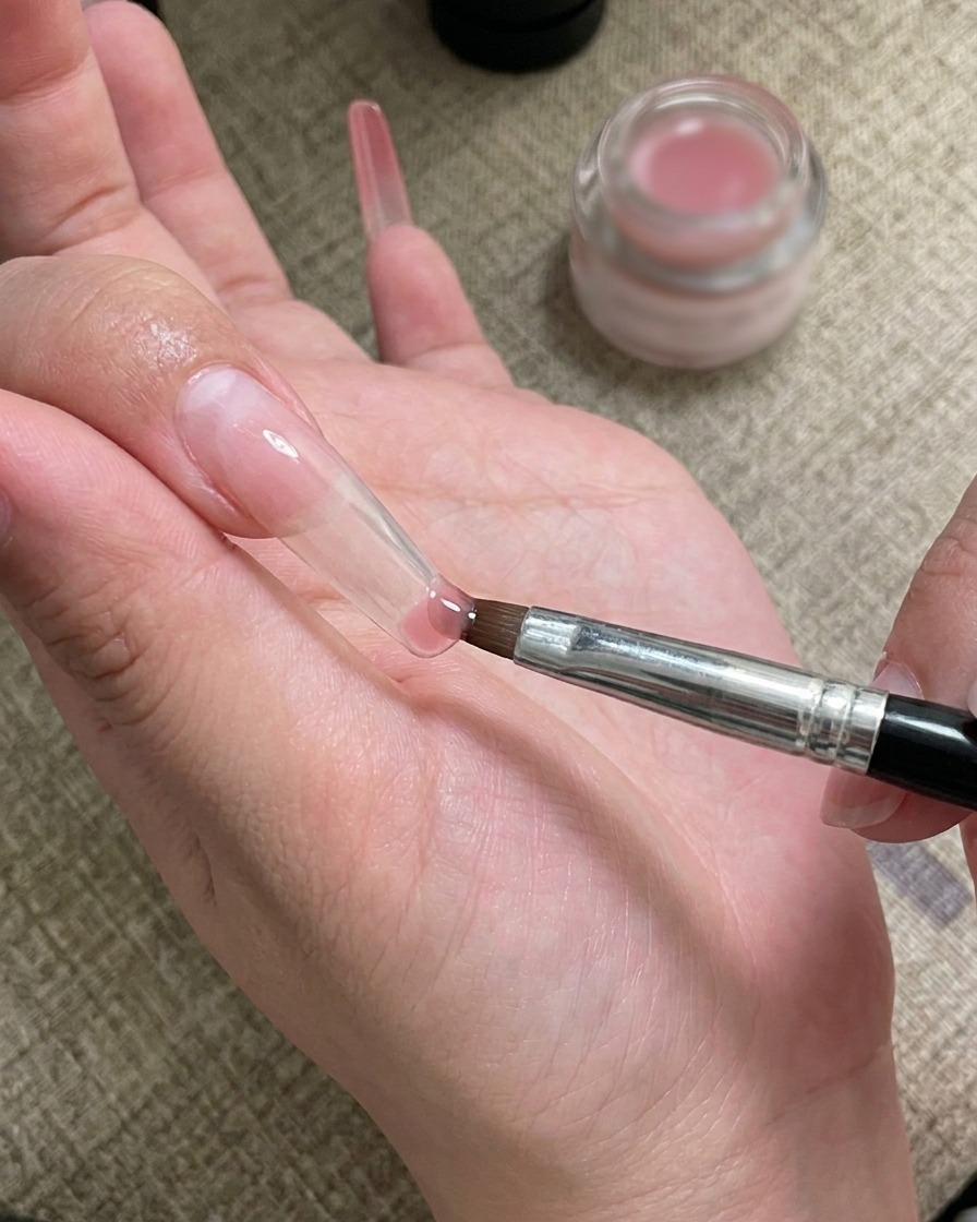 Ein Nail-Art-Pinsel beim Auftragen und Verblenden von Gel an der Nagelspitze.