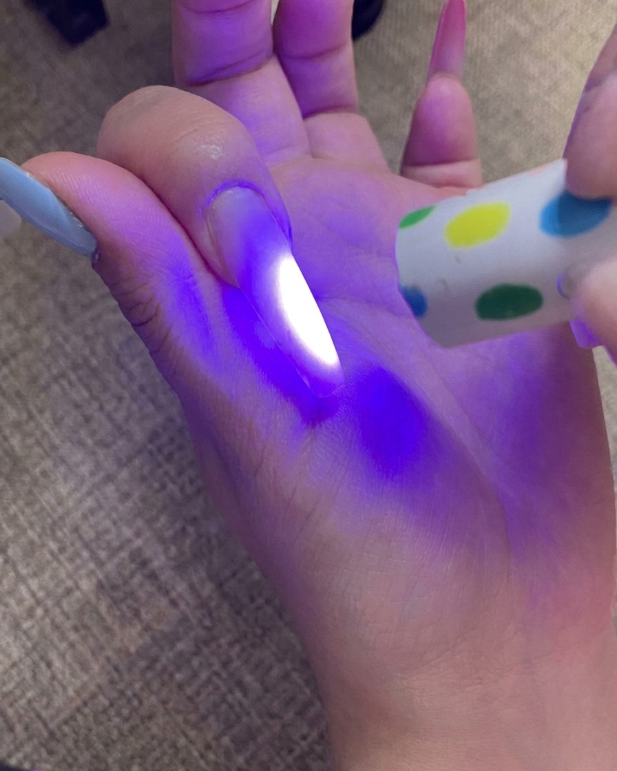 Eine Hand härtet den Nagel mit Ombré-Spitze unter einer UV-Lampe aus, wobei das Licht den Nagel beleuchtet.