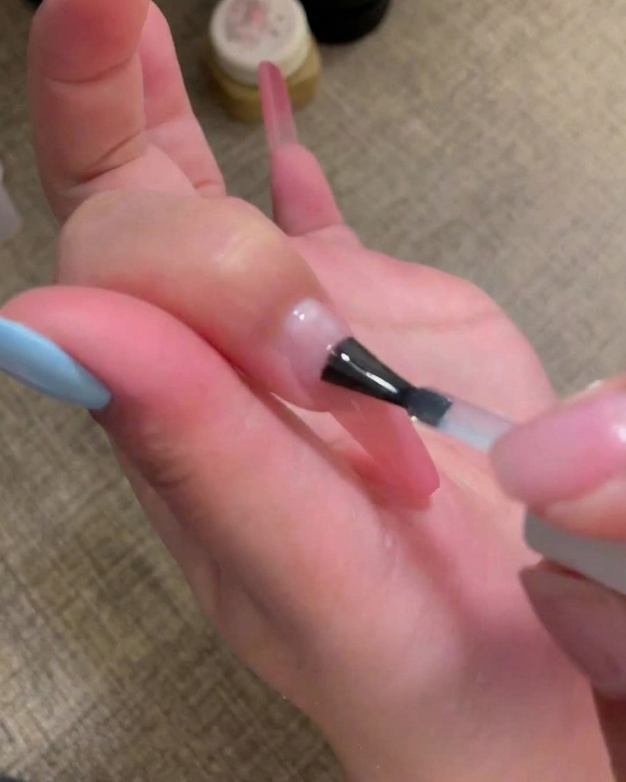 Ein Pinsel trägt einen klaren, glänzenden Base Coat auf die Nageloberfläche auf.