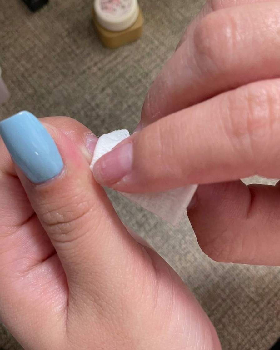 Eine Hand reinigt die Oberfläche eines manikürten Nagels mit einem fusselfreien Tuch.