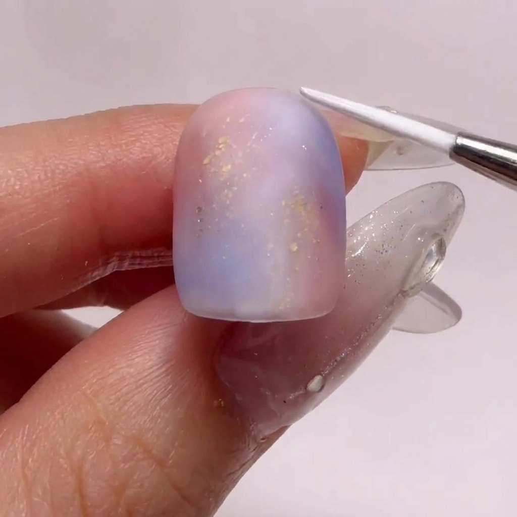 Ein Fine-Liner-Pinsel zeichnet zarte weiße Wellenmuster auf einen mattierten Nagel.