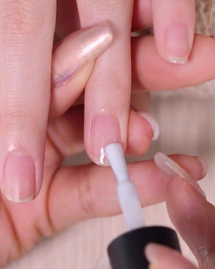 Nahaufnahme einer Hand, die eine Schicht transparenten weißen Lack auf einen Fingernagel aufträgt.