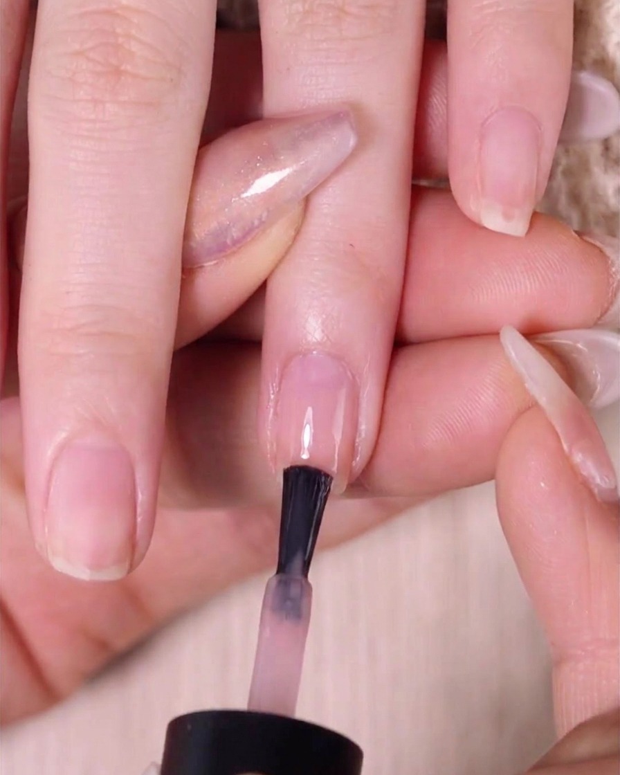 Ein Pinsel trägt eine zweite Schicht Nude-Pink auf die obere Hälfte des Nagels über die bereits verblendete Schicht auf.