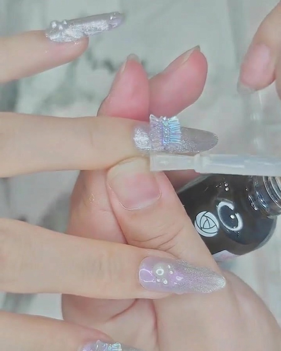 Ein Pinsel, der eine Schicht klaren, glänzenden Top Coat über den Nagel und die Perlenverzierungen aufträgt.