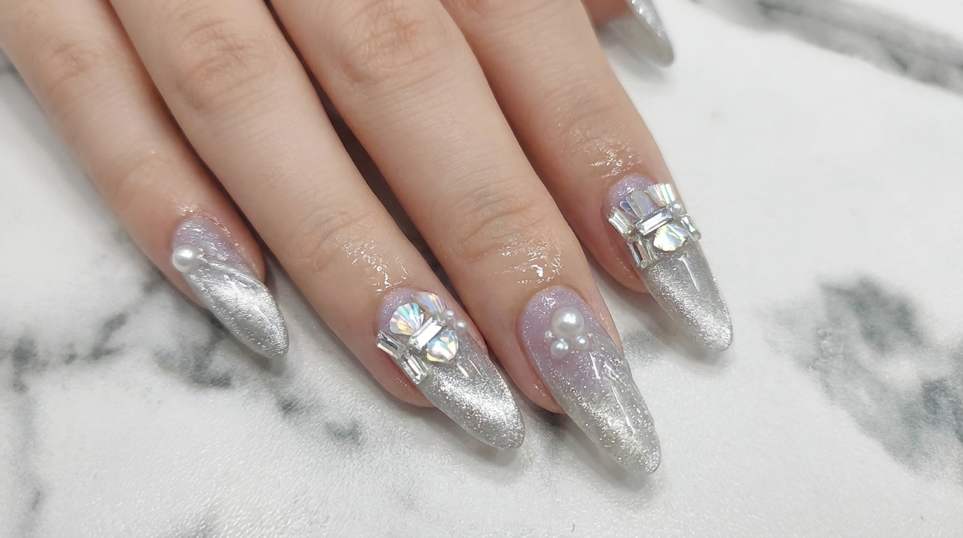 Lange mandelförmige Nägel mit einem halbtransparenten lila und silbernen magnetischen Cat-Eye-Farbverlauf, wunderschön verziert mit Perlen und Strasssteinen an der Nagelhaut.