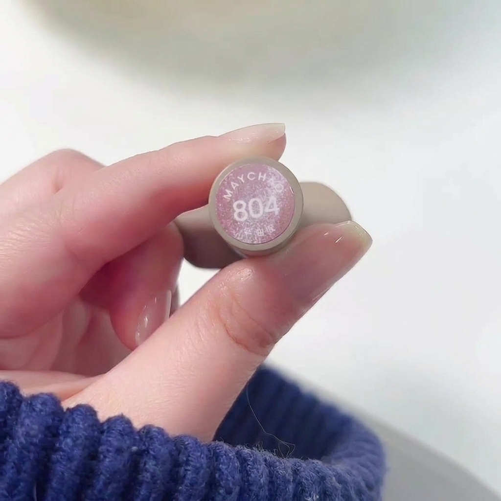 Eine Nahaufnahme einer Hand, die die Flasche Meichao 804 Taozhi Yaoyao hält, während der schimmernde Nude-Pink-Lack auf einen Fingernagel aufgetragen wird.