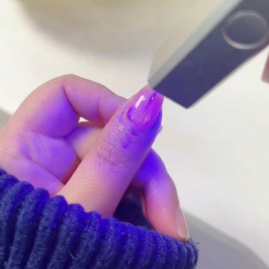 Ein Finger mit feuchtem, schimmerndem lila Gel-Lack in einer leuchtenden UV/LED-Nagellampe.