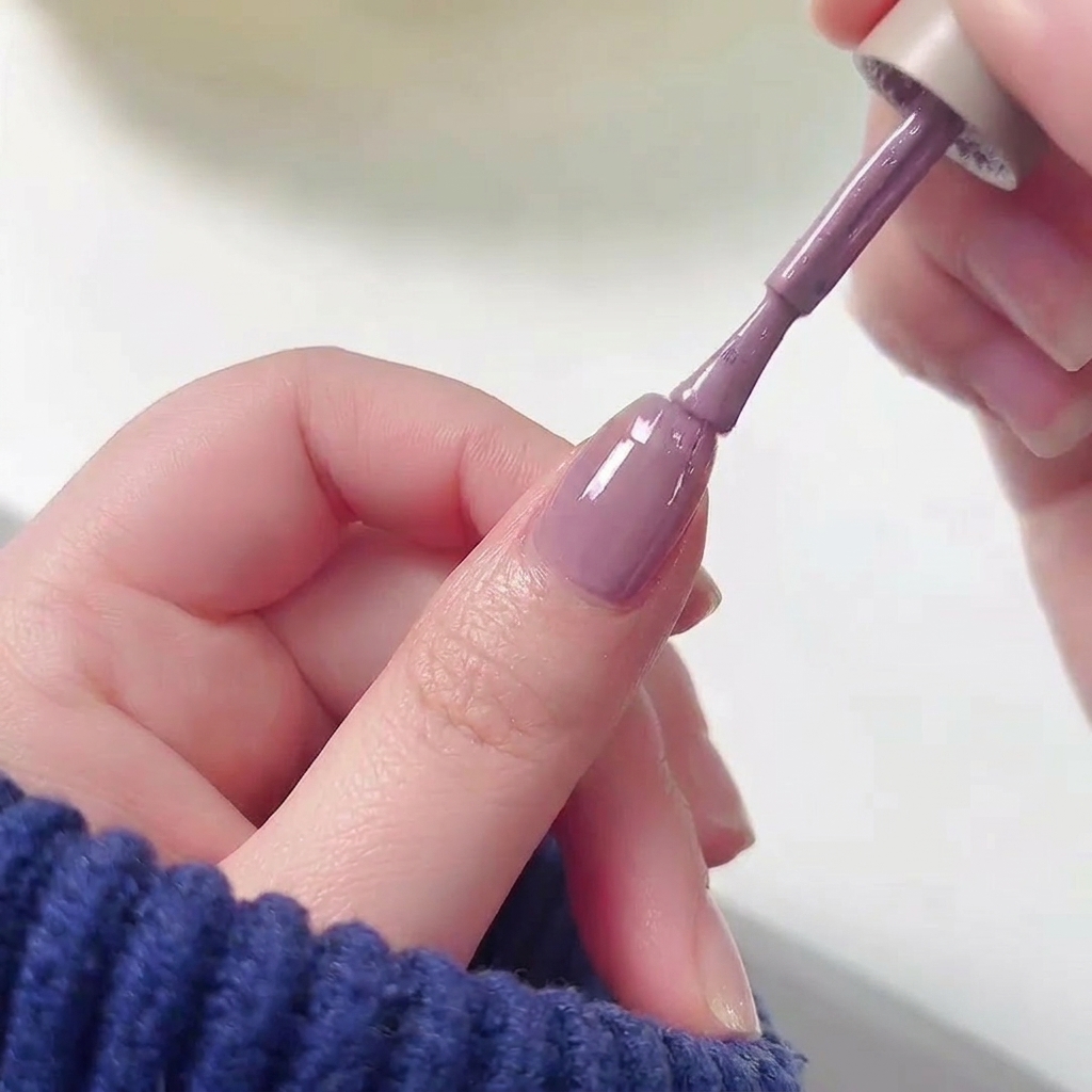 Ein Nagellackpinsel, der lila Gel-Lack auf die obere Hälfte eines Fingernagels über einer rosa Basis aufträgt.