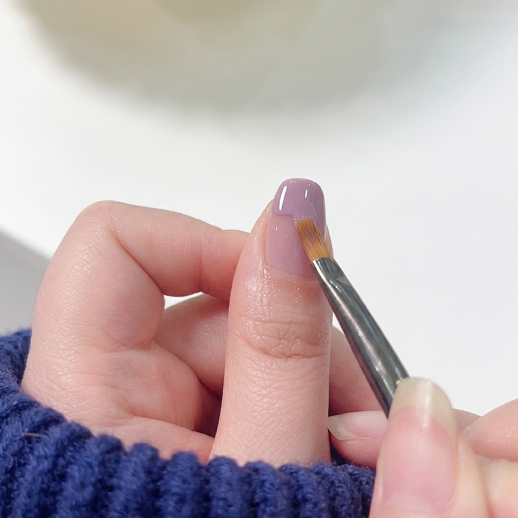 Ein flacher Nail Art Pinsel streicht sanft über die untere Kante des lila Lacks nach unten in eine rosa Basis, um einen nahtlosen Übergang zu schaffen.