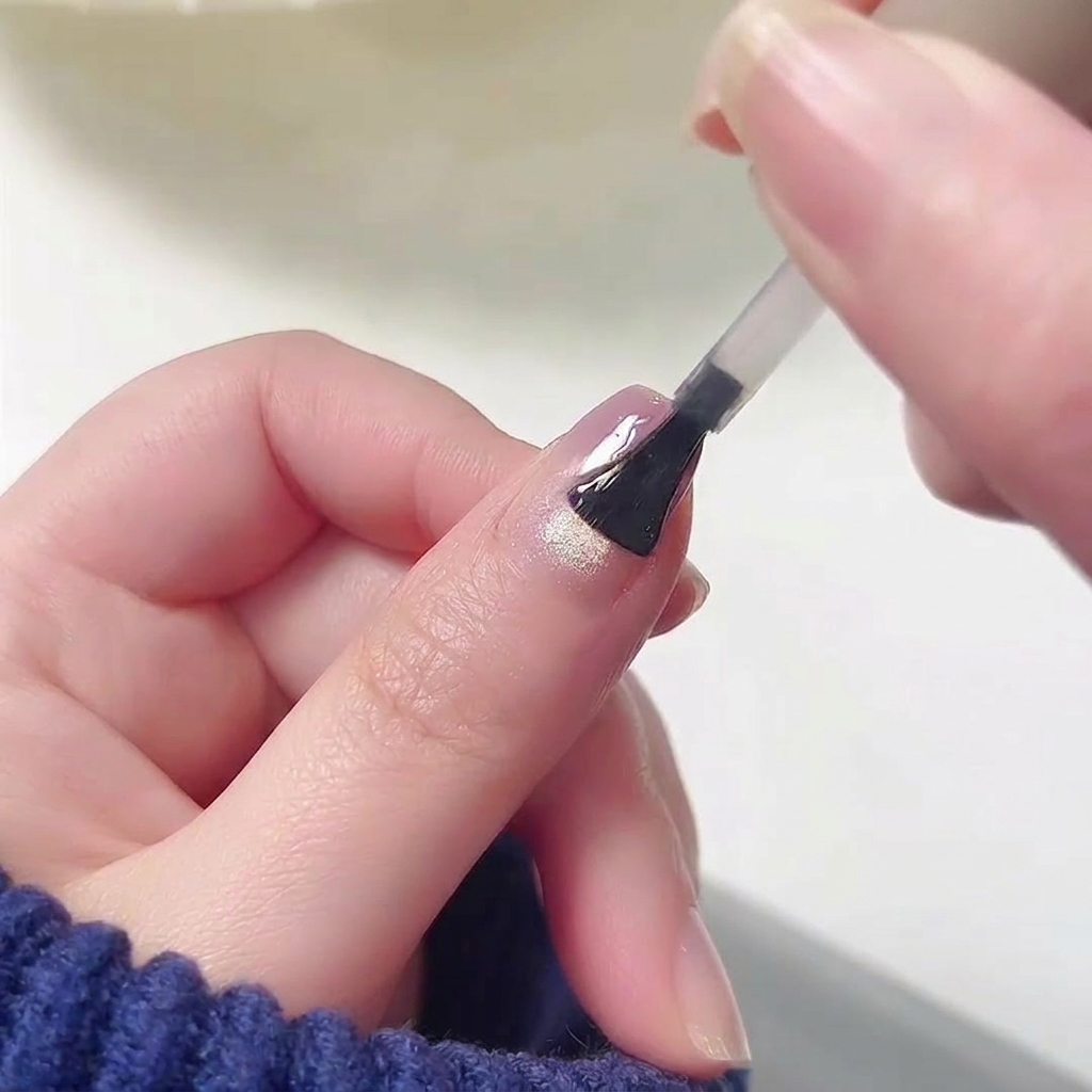 Ein Pinsel trägt einen klaren, hochglänzenden Top Coat auf die Oberfläche eines Nagels auf, der bereits ein nahtloses pink-lila Ombré-Design aufweist.