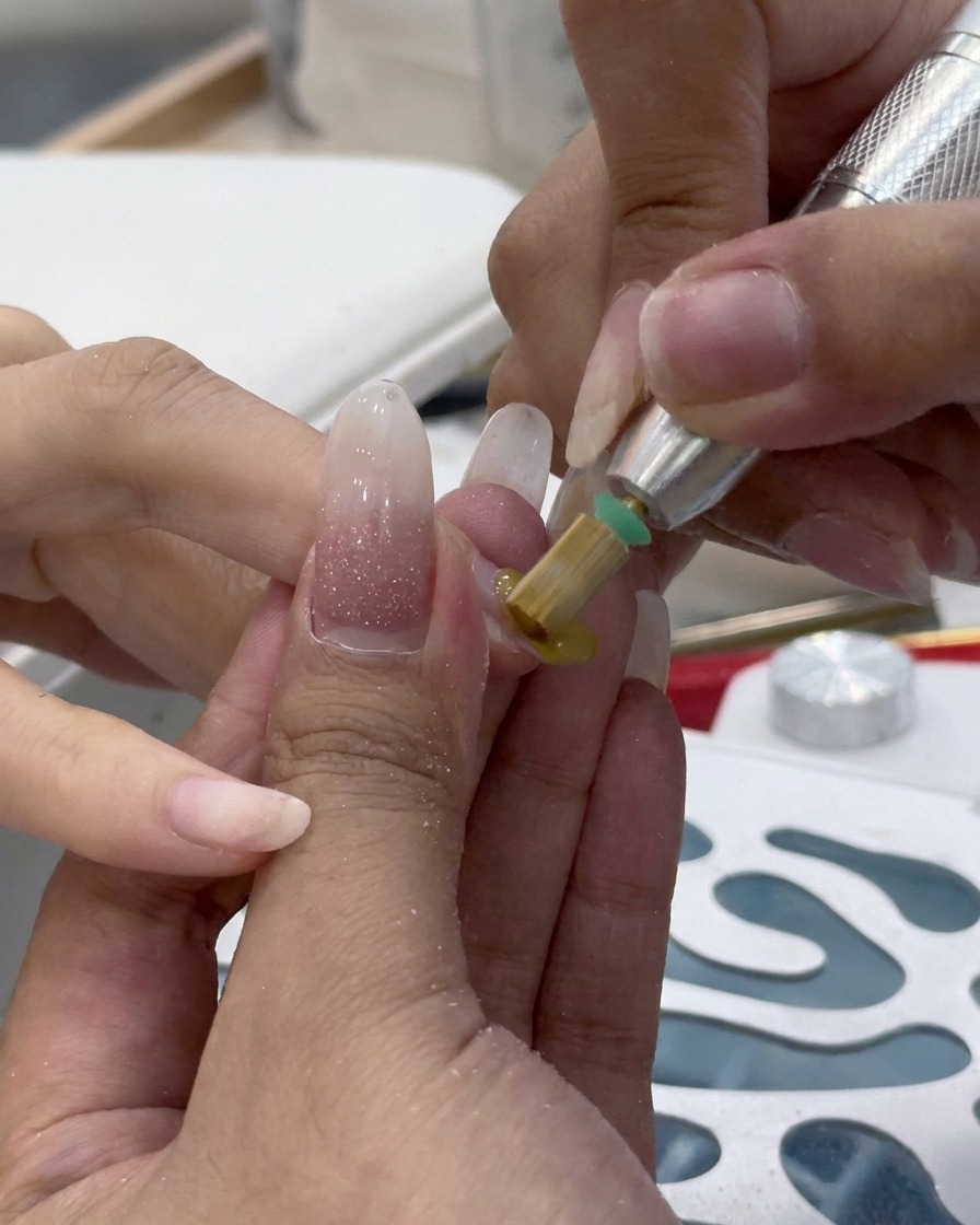 Nahaufnahme eines elektrischen Nagelfräsers mit Schleifband beim Entfernen von altem Gelmaterial.