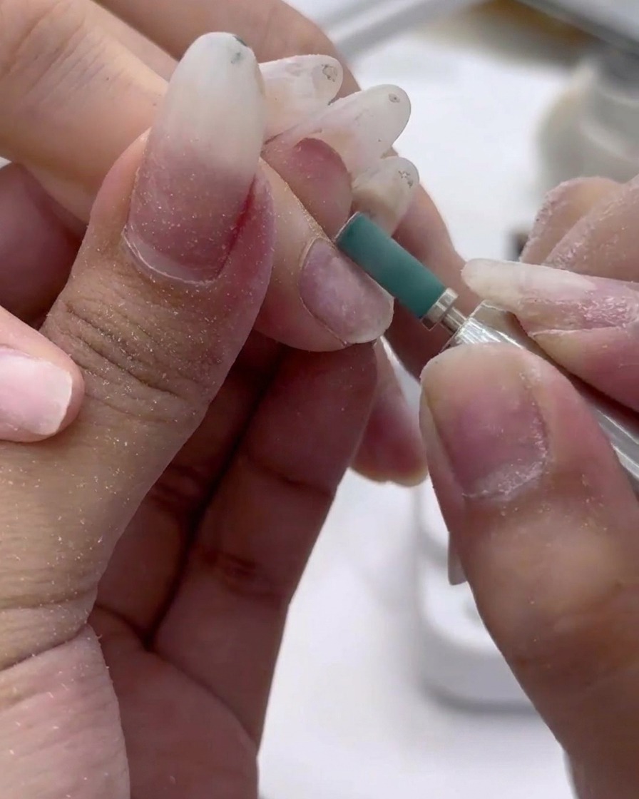 Nahaufnahme eines grünen Schleifbandes, das sanft die Oberfläche des Naturnagels anmattiert.