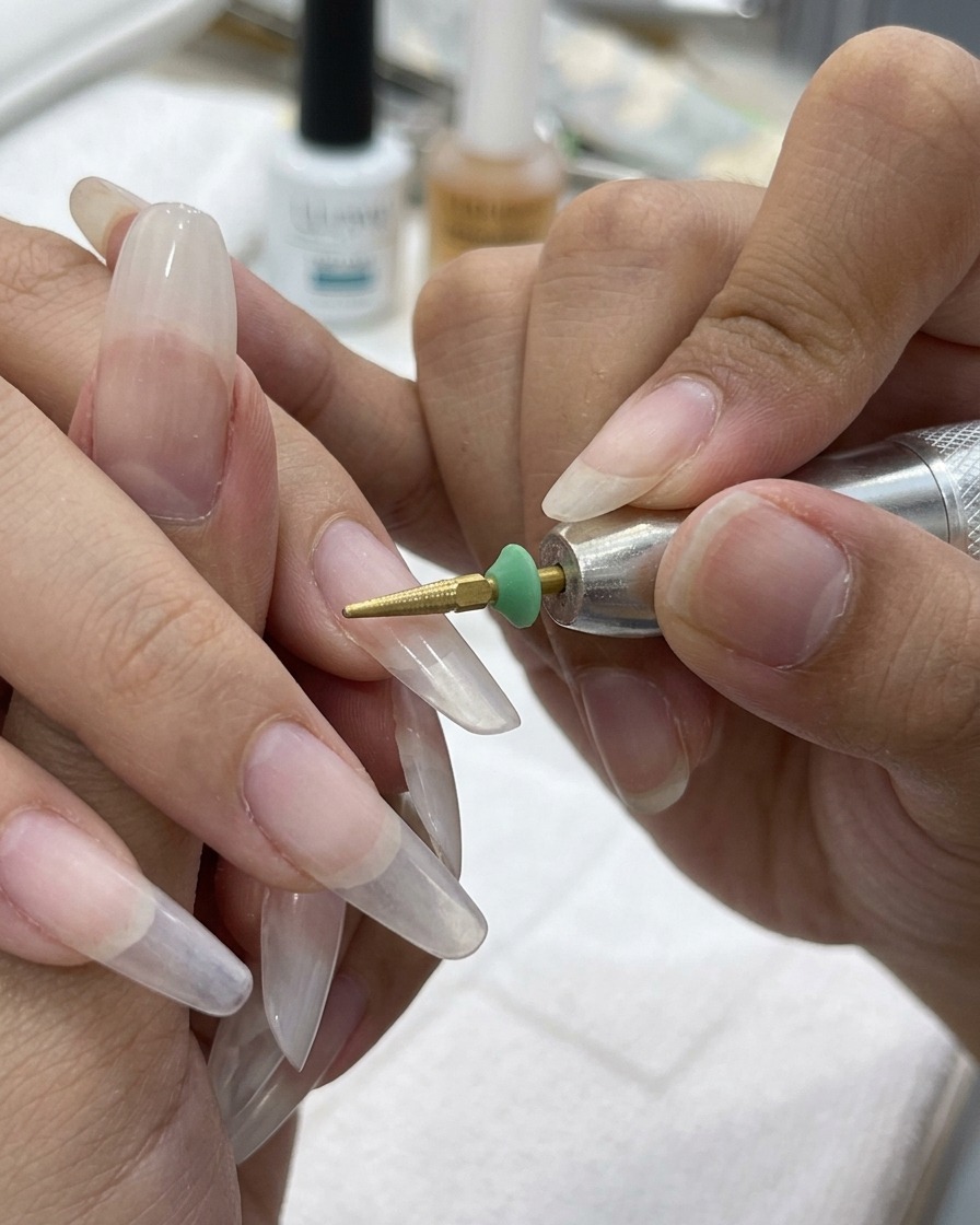 Ein goldener, kegelförmiger Fräseraufsatz glättet den Übergang zwischen der Nagelspitze und dem Naturnagel.