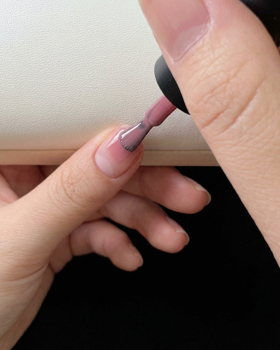 Eine Nahaufnahme, wie ein Pinsel rosa Farbgel auf die Spitze eines natürlichen Fingernagels aufträgt.