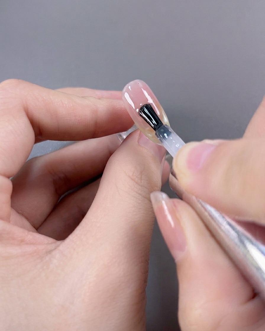 Ein Pinsel trägt als letzten Schritt einen hochglänzenden Top Coat über eine fertige Cat-Eye-French-Maniküre auf.