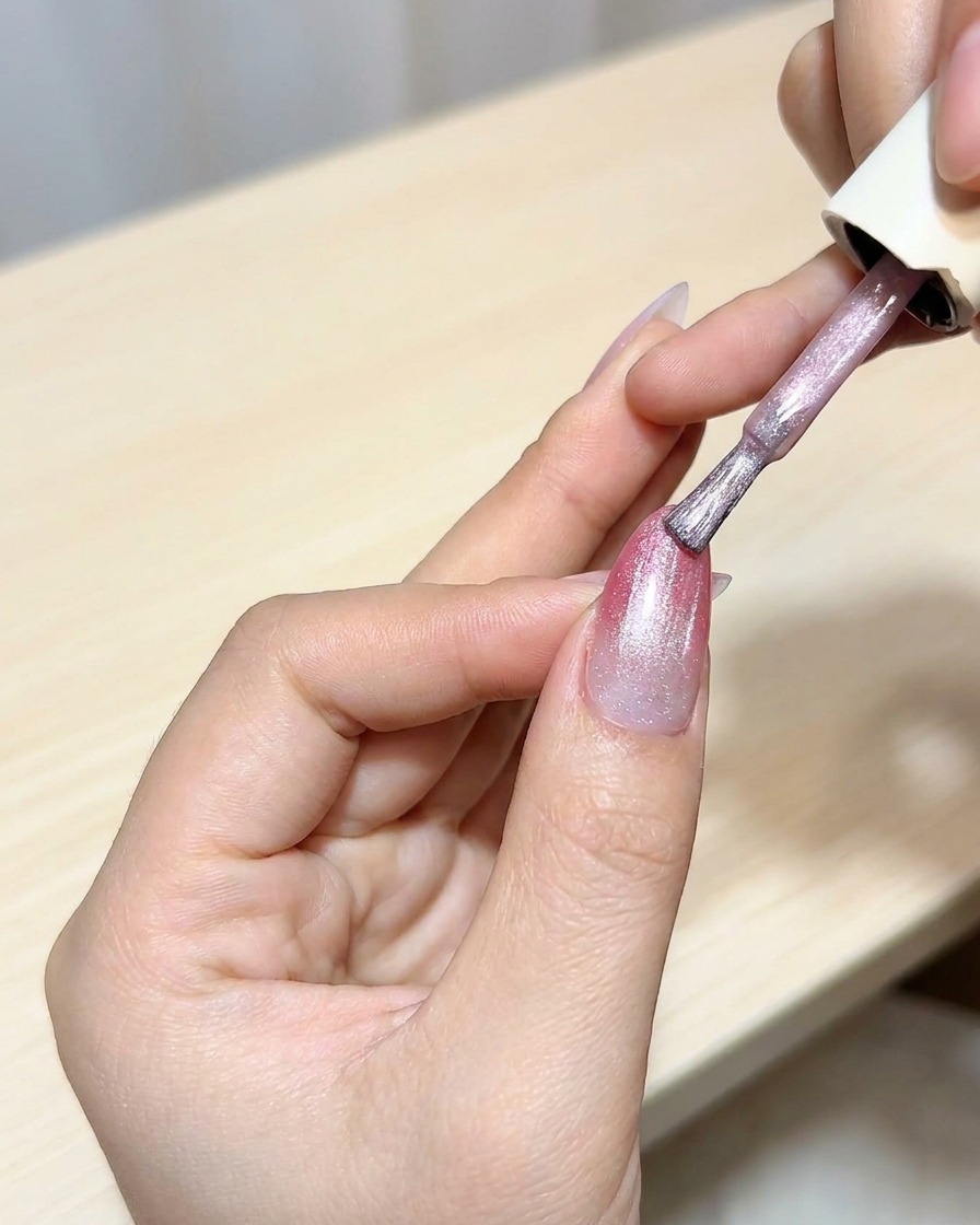 Ein Pinsel trägt eine Schicht Cat-Eye-Gel über der magentafarbenen Ombré-Basis auf.
