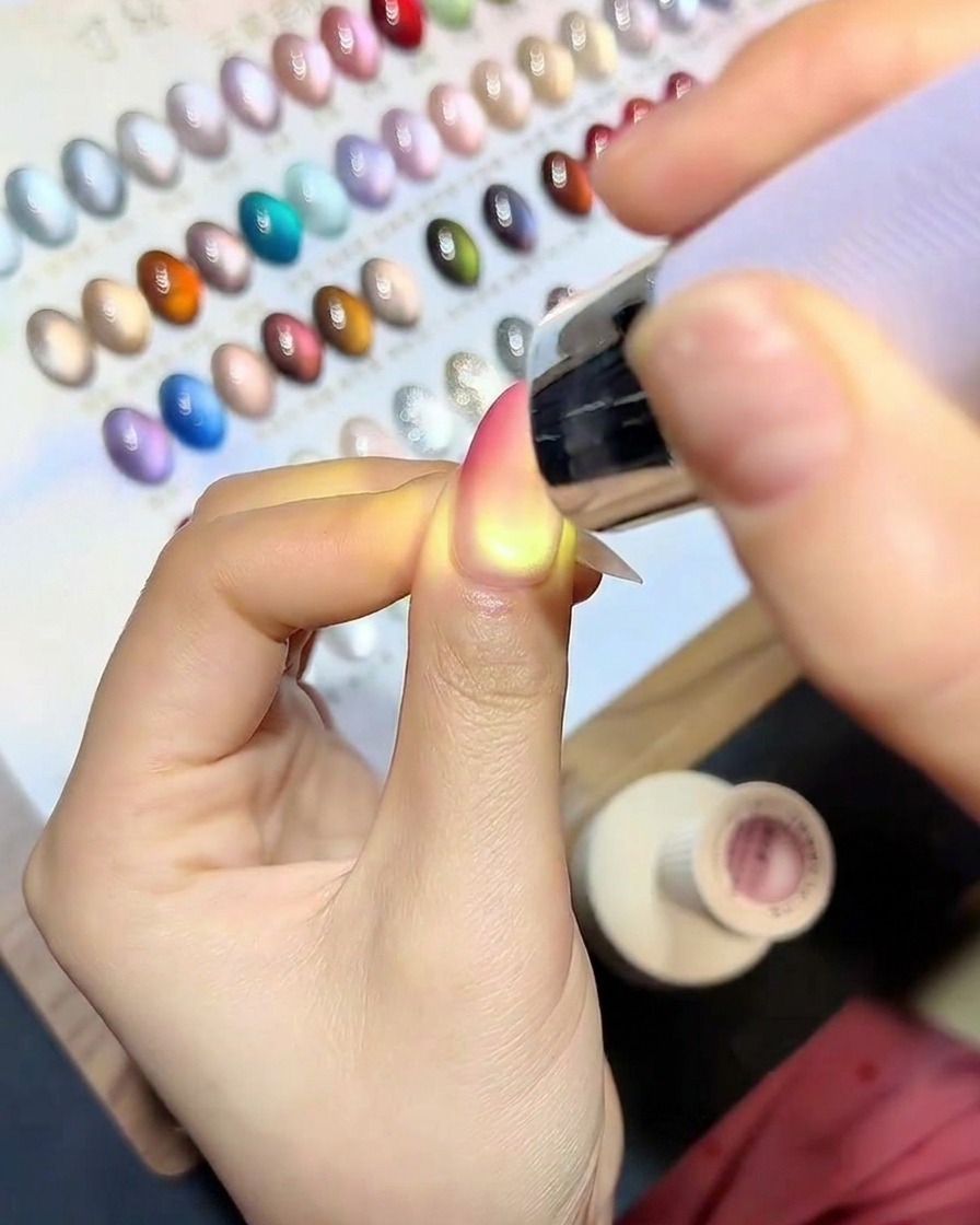 Ein Pinsel trägt ein klares, glänzendes Versiegelungsgel über dem fertigen Cat-Eye-Gradient-Nagel auf.