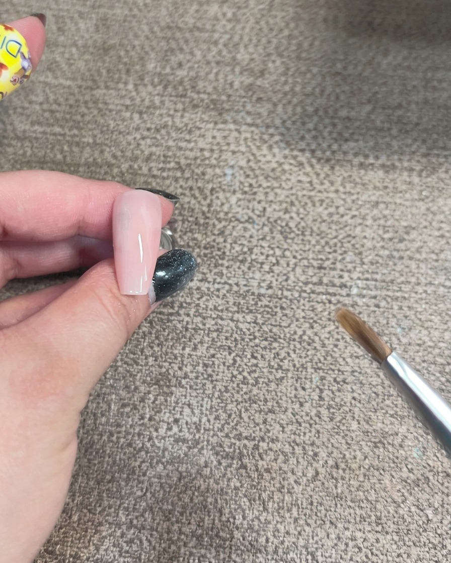 Nahaufnahme eines Pinsels, der irisierendes Gel in geschwungener Form auf eine hellrosa Nagelbasis aufträgt.