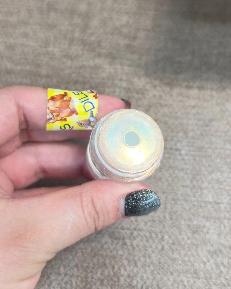 Ein kleines Döschen mit Aurora-Nagelpuder, das einen multidimensionalen gelben und blauen Schimmer zeigt.