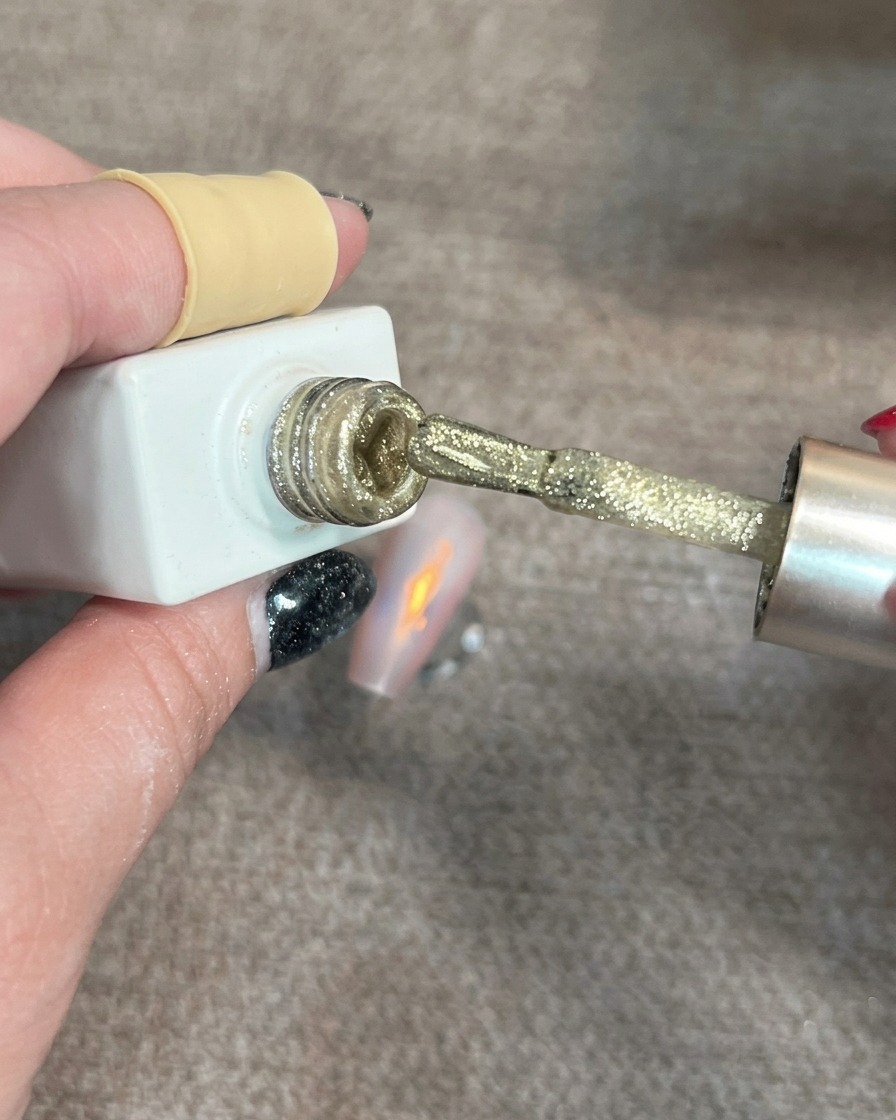 Ein Nagelpinsel, der kleine, schimmernde Cat-Eye-Gel-Punkte auf einen teilweise dekorierten Nagel aufträgt.