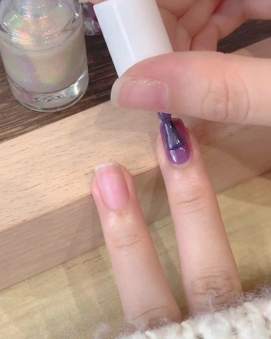 Nahaufnahme eines Pinsels, der tiefvioletten Gellack auf einen Naturnagel aufträgt.