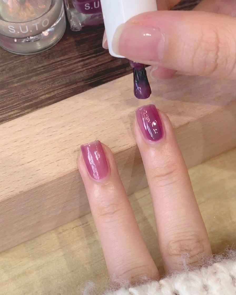 Nahaufnahme eines Pinsels, der die Oberfläche des violetten Lacks auf dem Nagel glättet.