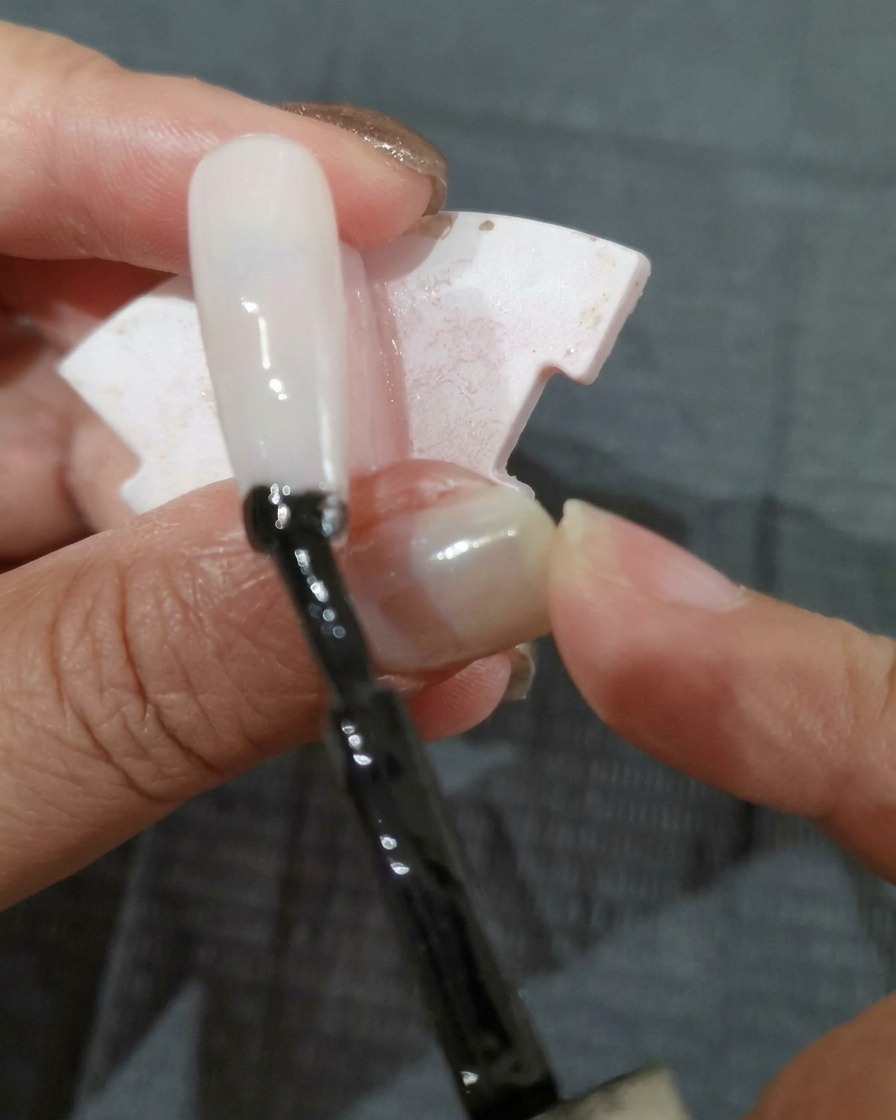 Ein Pinsel trägt eine Schicht schwarzes Gel auf eine Nagelspitze auf.