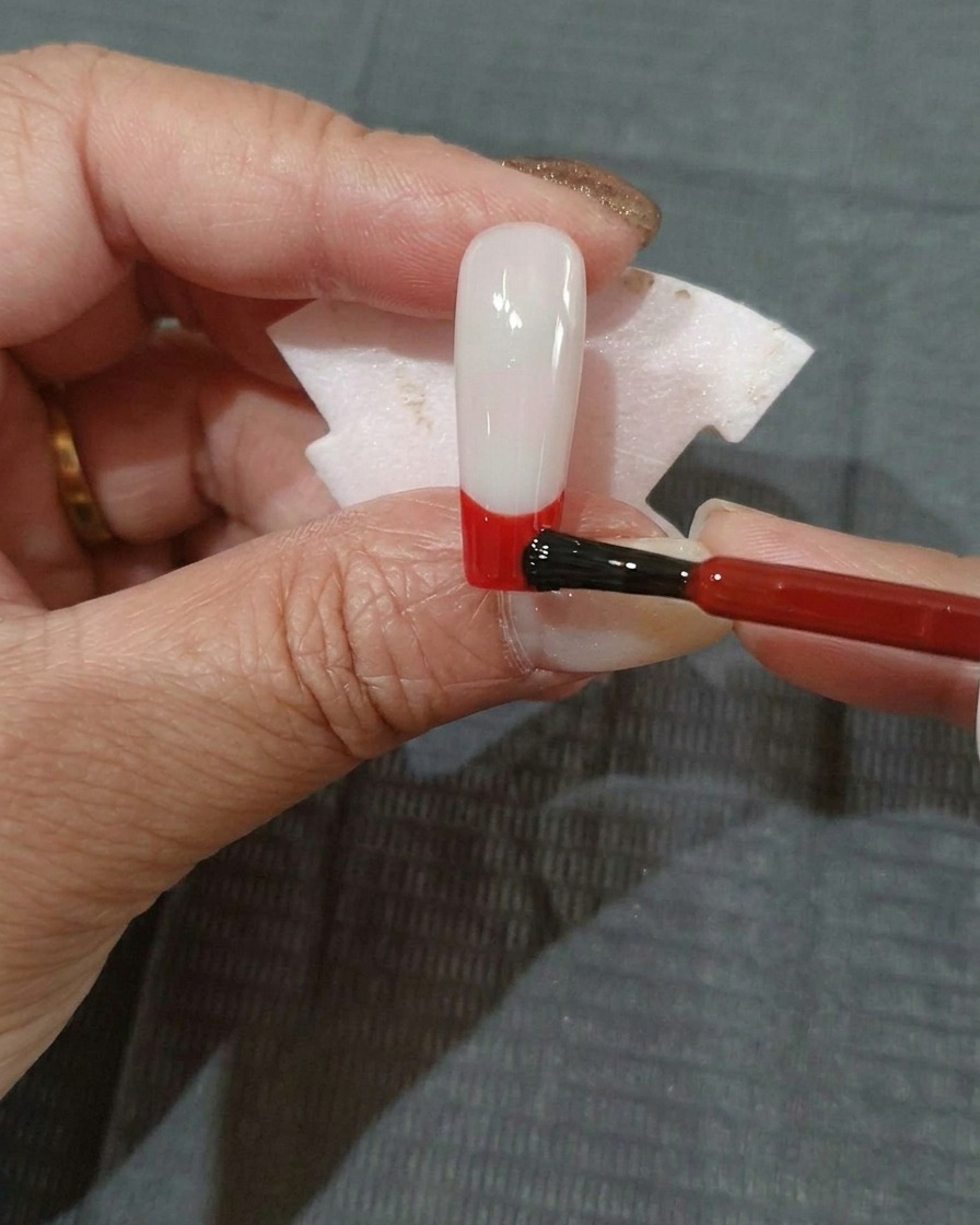 Eine dünne Schicht rotes Gel wird auf den unteren Bereich eines schwarz grundierten Nagels aufgetragen.