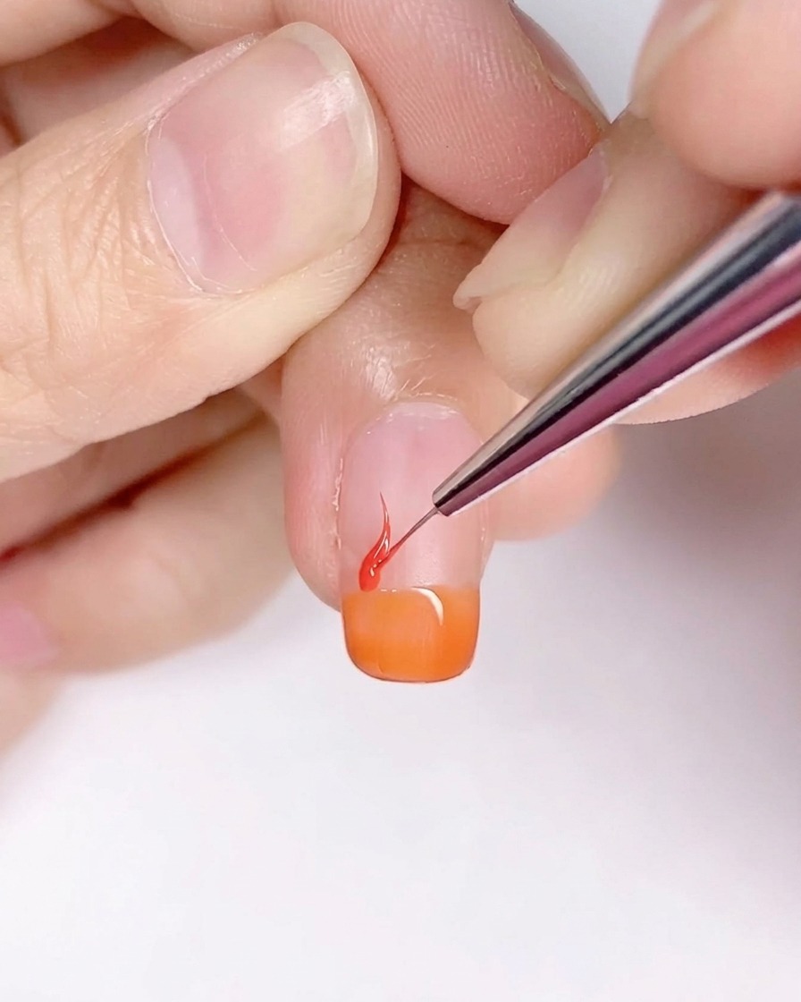 Ein feiner Detailpinsel zeichnet flammenartige Formen auf den orange grundierten Nagel.