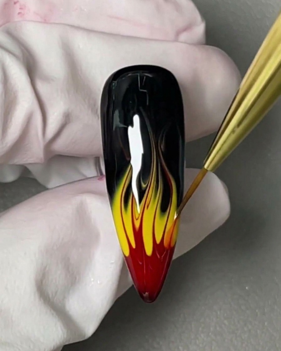 Ein kleiner Pinsel trägt ein klares, viskoses Blooming Gel auf einen schwarz lackierten Nagel auf.