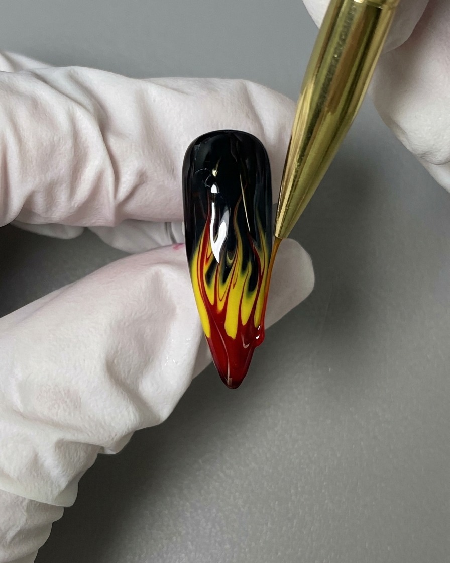 Ein Liner-Pinsel trägt einen glänzenden Überlack auf das fertige Flammen-Design auf.