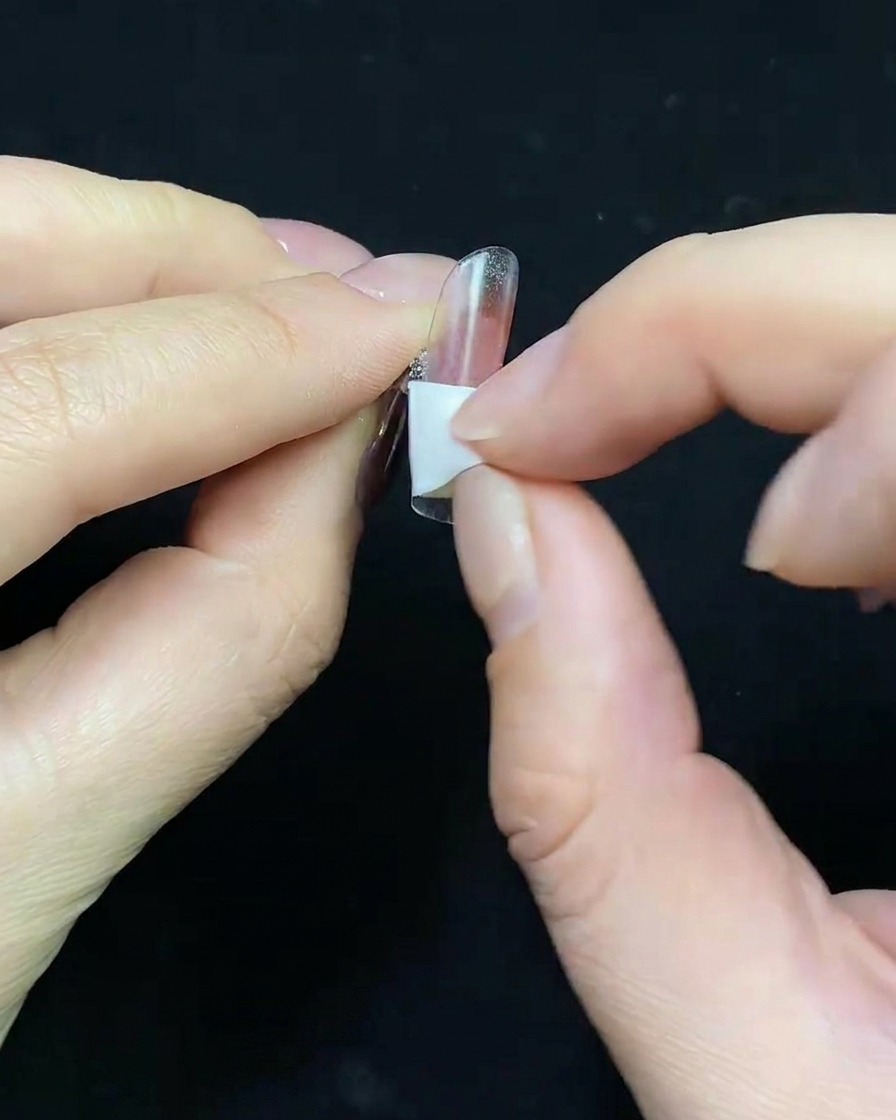 Nahaufnahme eines Pinsels, der ein nudefarbenes Gel als Basis auf einen transparenten Nagel-Tip aufträgt.