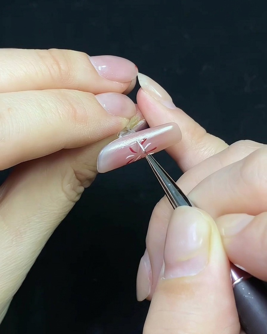 Ein feiner Pinsel trägt Top Coat auf einen Nagel mit Feuerwerksdesign und einer kleinen Perlenverzierung auf.