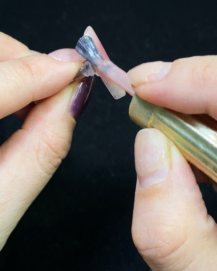 Ein Pinsel trägt eine dünne Schicht Nude-Gel auf einen transparenten Nagel-Tip auf.