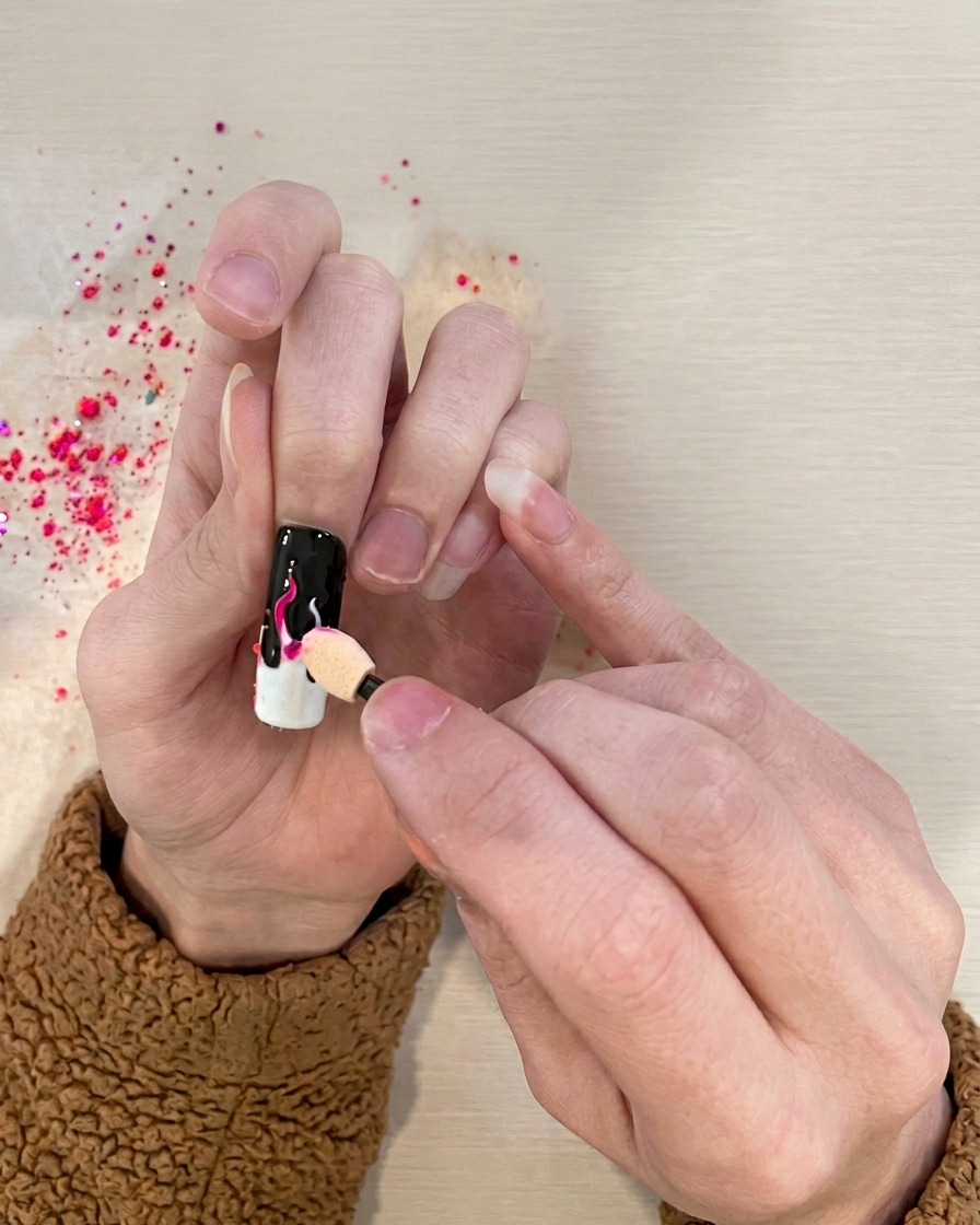 Ein Schwammapplikator tupft kräftiges pinkes Pigment auf die weißen Flammendetails des Nagels.