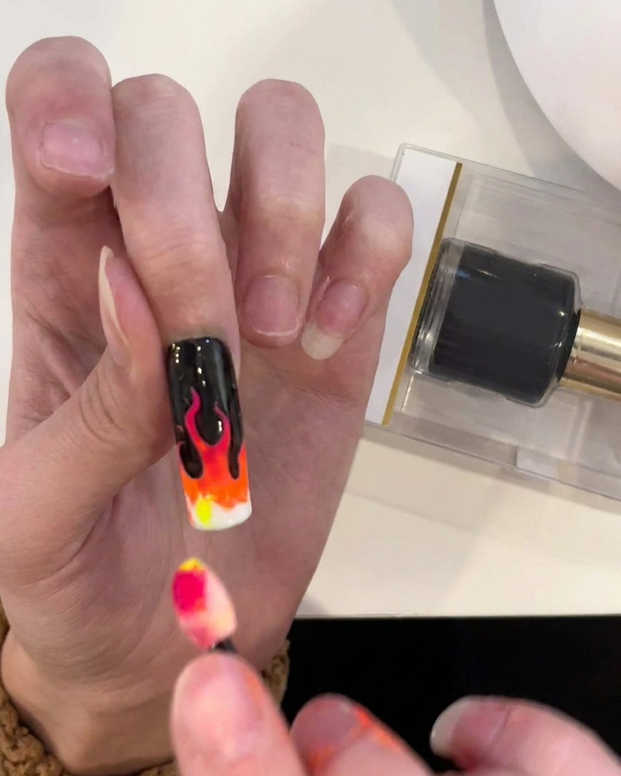Ein Schwammapplikator trägt gelbes Pigment auf den letzten Abschnitt des Flammen-Farbverlaufs an der Nagelspitze auf.