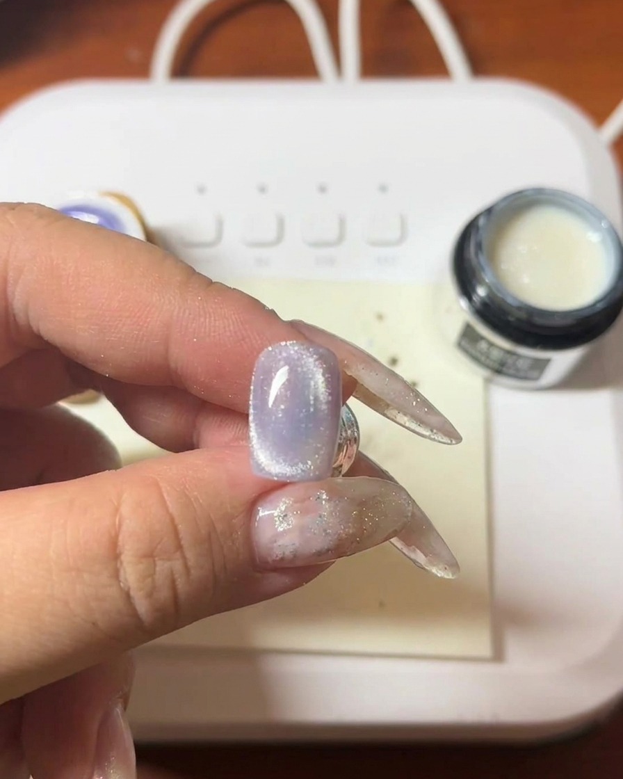 Ein Magnetstab wird über einem violetten Cat-Eye-Nagel gehalten, wobei der helle Cat-Eye-Streifen sichtbar wird.