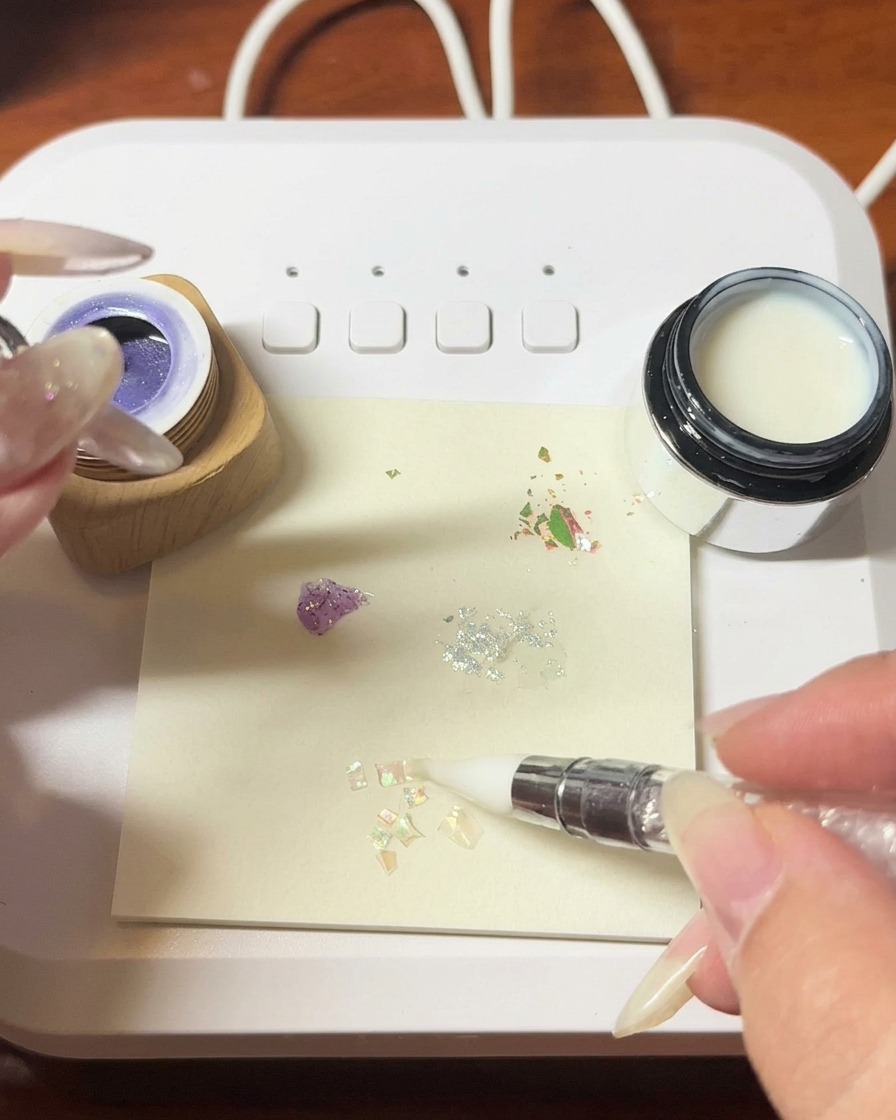Eine Pinzette platziert zarte, irisierende Muschelfragmente auf einer feuchten Geloberfläche.