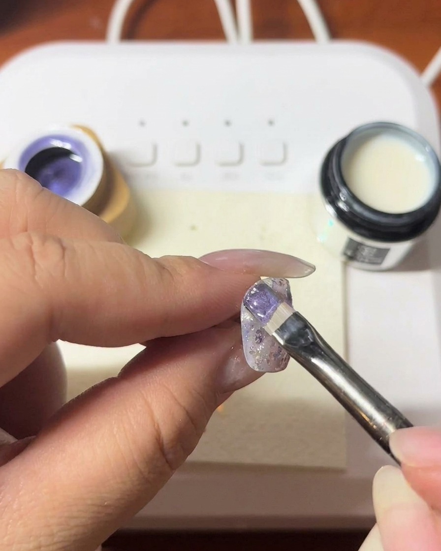 Ein Magnetwerkzeug wird in der Nähe eines Nagels gehalten, um einen schimmernden Cat-Eye-Streifen im violetten Gel zu erzeugen.