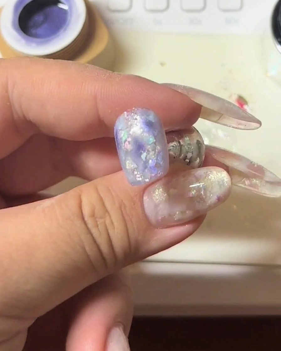 Ein Nagel mit violettem Cat-Eye-Gel wird unter einen Magneten gehalten, um den schimmernden Lichtstreifen zu intensivieren.
