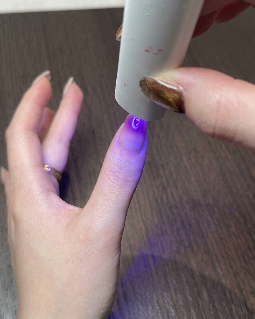 Eine Hand unter einer kleinen UV-Lampe härtet das fertige magnetische Cat-Eye-Nageldesign aus.