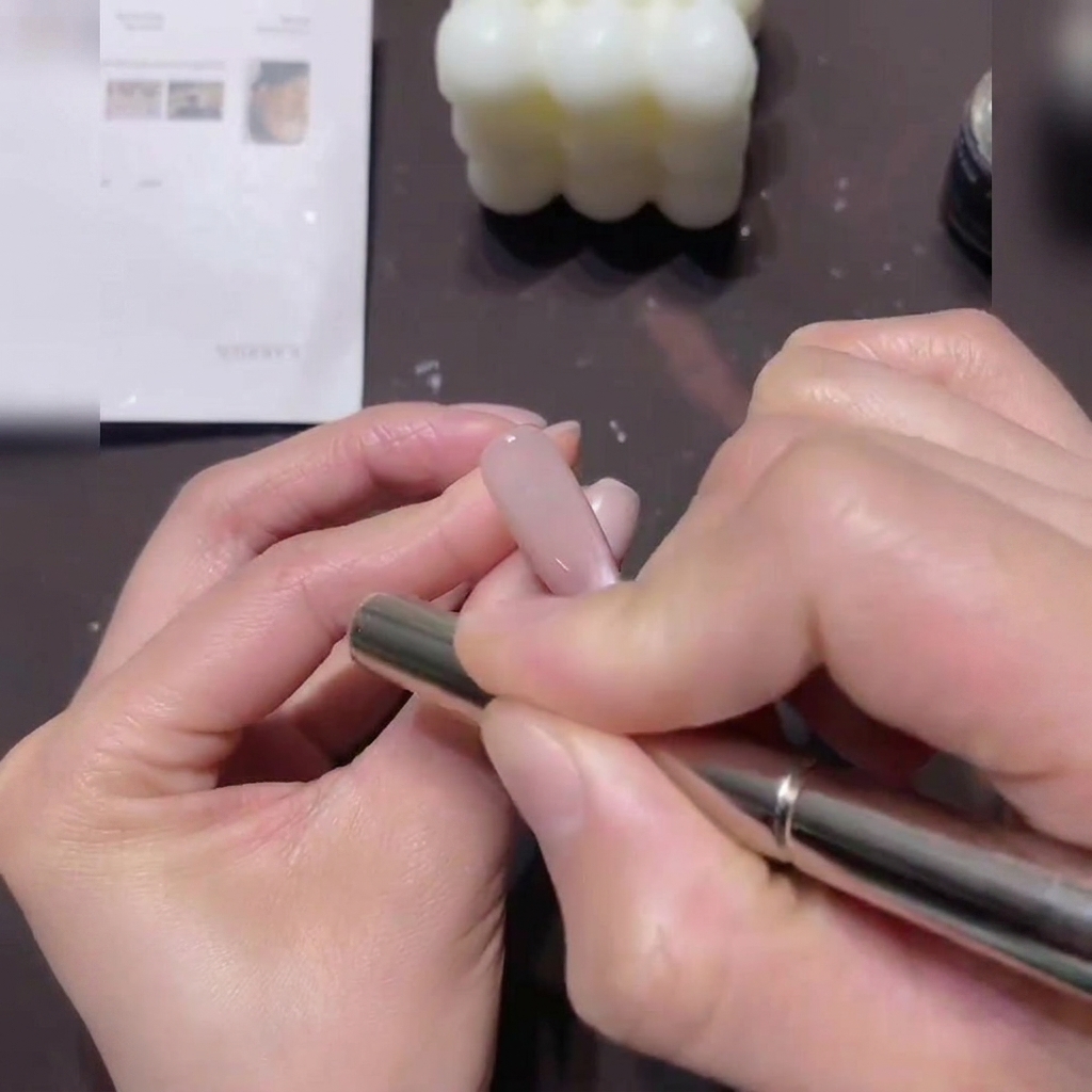 Eine Hand hält einen zylindrischen Magneten und bewegt ihn in kreisenden Bewegungen um den Rand eines mit Cat-Eye-Gel lackierten Nagels.