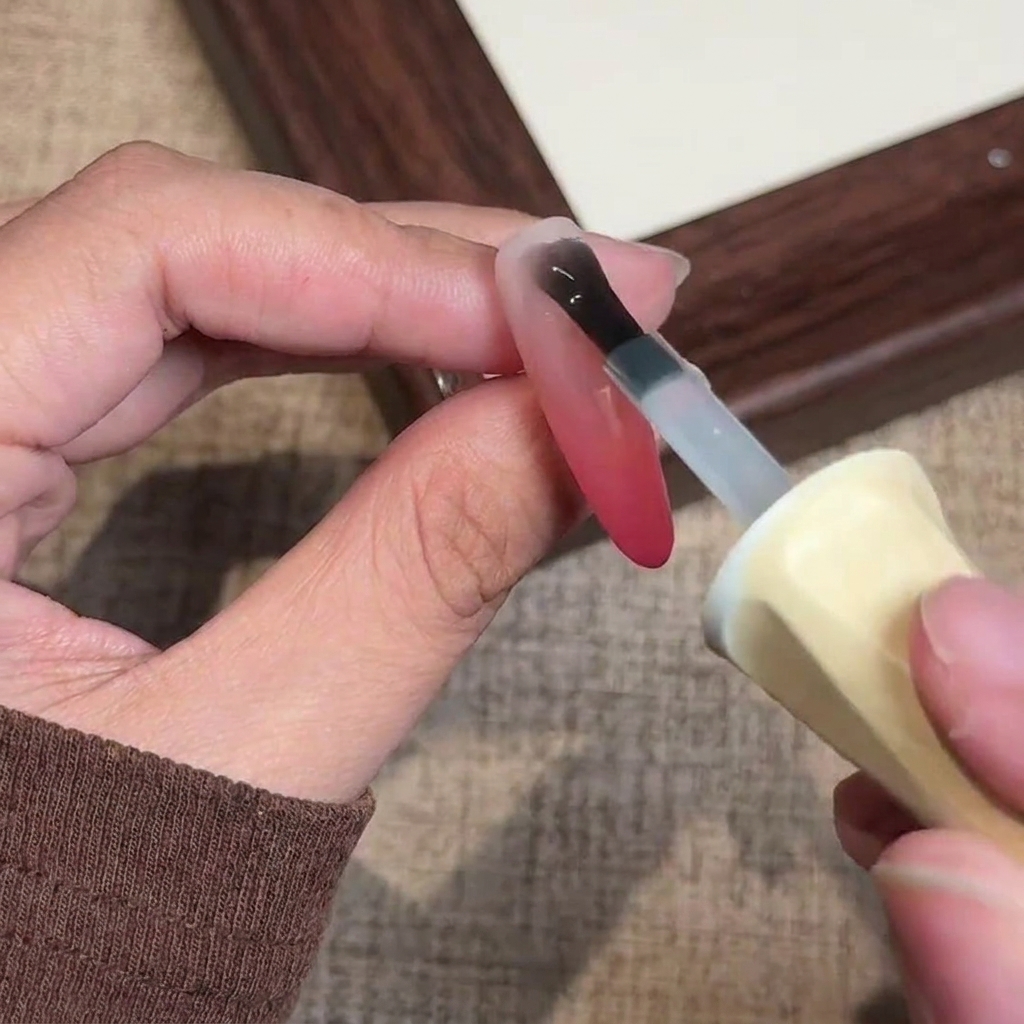 Ein Pinsel trägt einen finalen matten Gel-Überlack auf den fertigen Ombré-Nagel auf.