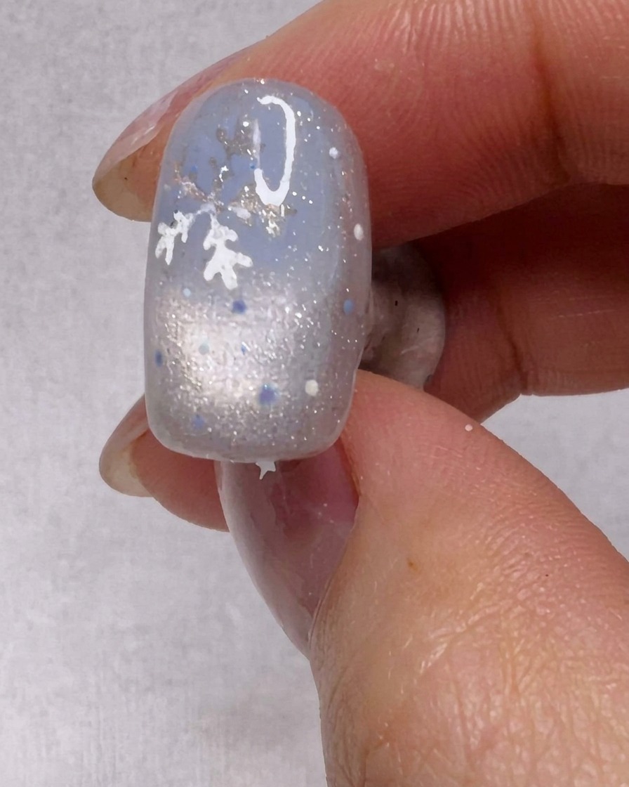 Ein Pinsel trägt eine Schicht schimmernden silbernen Gellack auf einen Nagel auf.