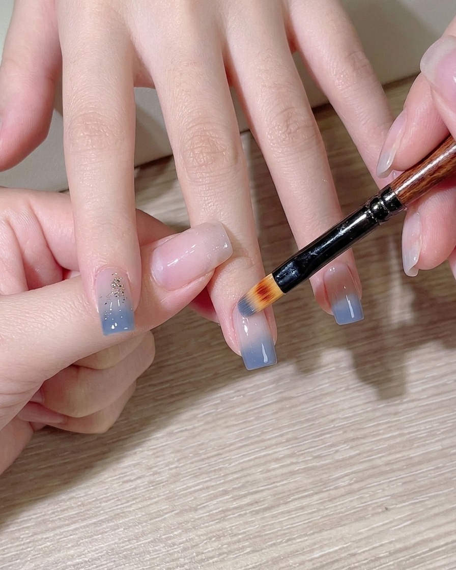 Ein Make-up-Schwämmchen tupft hellblauen Lack auf einen Fingernagel.