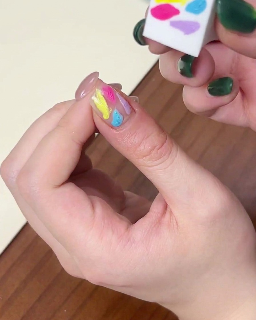 Nahaufnahme einer Seite eines Schwämmchens, das verwendet wird, um bunte Gellack-Punkte auf einem Nagel zu verblenden.
