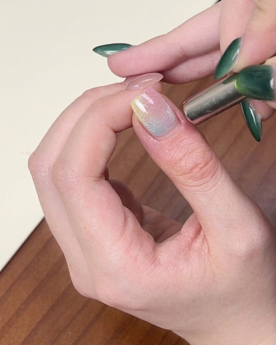 Ein zylindrischer Magnet wird seitlich an einen Fingernagel gehalten, um das schimmernde Cat-Eye-Gellack zu stylen.