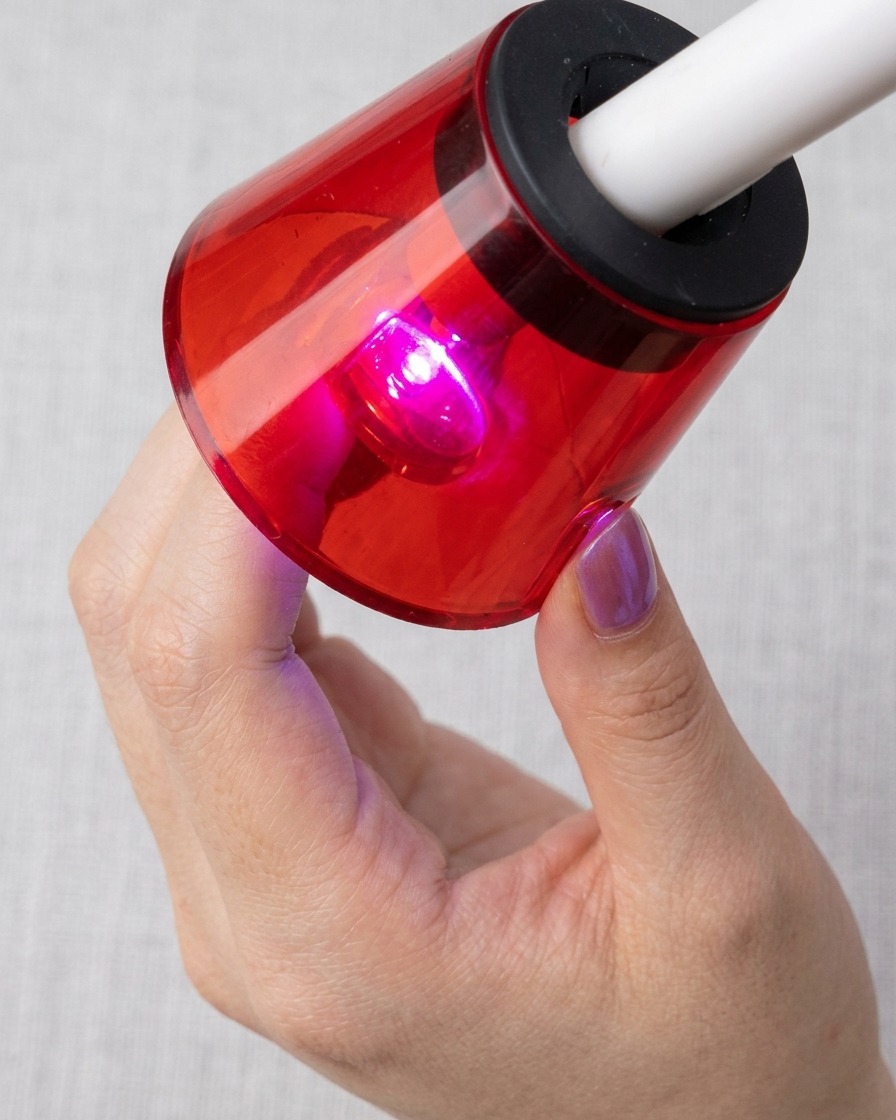 Ein Fingernagel unter einer roten UV/LED-Lampe, während das Cat-Eye-Muster zu sehen ist.