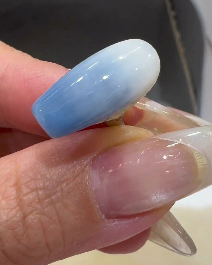 Ein Pinsel trägt eine dünne Schicht milchig-weißen UV-Nagellack auf einen transparenten Nageltip auf.